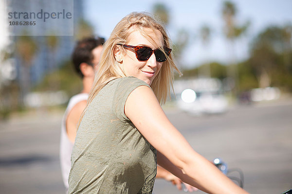 Junge Frau  die sich beim Radfahren mit ihrem Freund in Venice Beach  Los Angeles  Kalifornien  USA  über die Schulter schaut