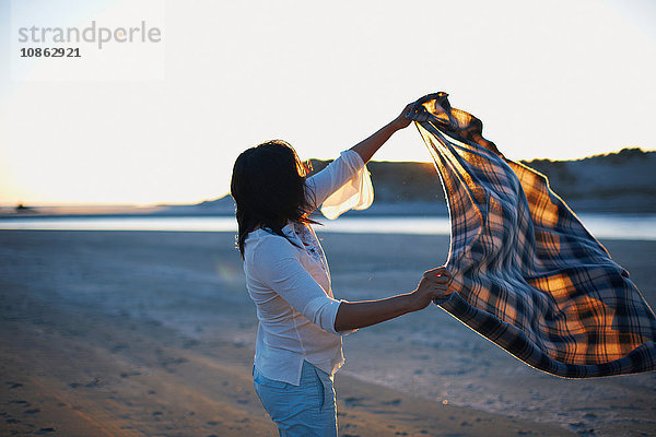 Frau schüttelt bei Sonnenuntergang Decke am Strand  Cannon Beach  Kalifornien  USA