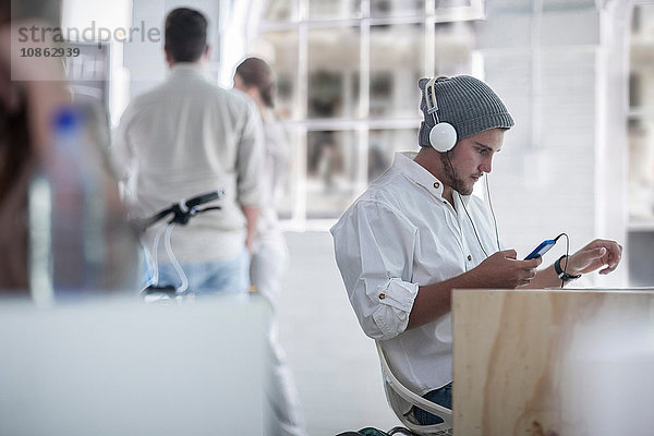Geschäftsmann benutzt Smartphone mit Kopfhörern im Loft-Büro