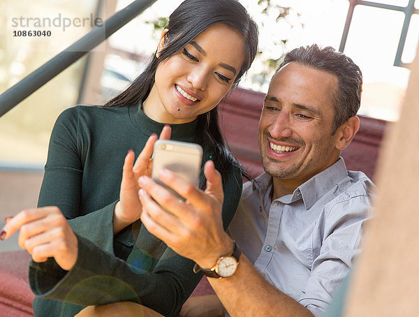 Paar sitzt auf einer Treppe und benutzt ein Smartphone und lächelt