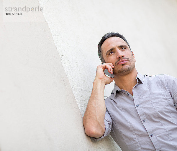 Niedriger Blickwinkel auf einen an die Wand gelehnten Mann  der mit einem Smartphone telefoniert