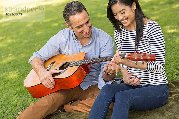 Auf Gras sitzendes Ehepaar spielt Akustikgitarre und lächelt