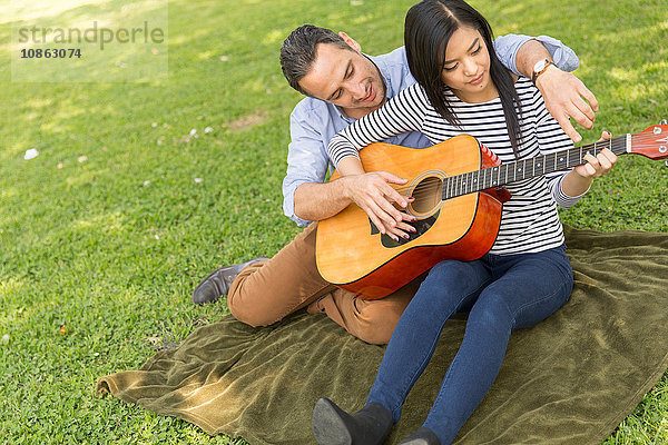 Mann sitzt auf Gras und lehrt Frau Akustikgitarre spielen
