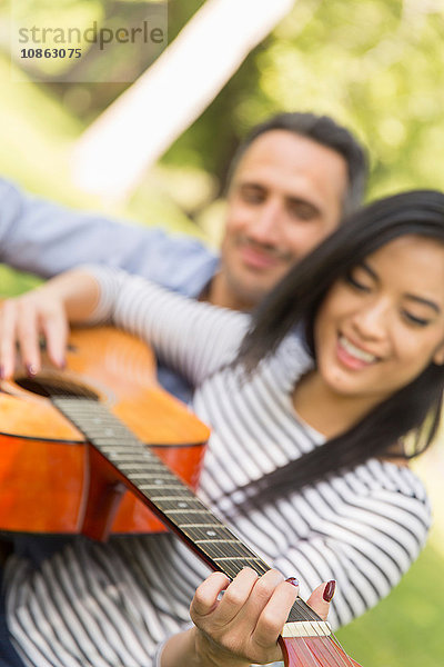 Frau sitzt auf Gras und spielt akustische Gitarre lächelnd