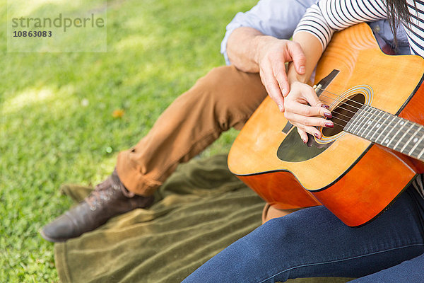 Ausschnitt eines Paares  das auf Gras sitzt und akustische Gitarre spielt