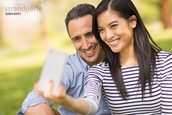 Paar sitzt auf dem Rasen und benutzt ein Smartphone  um sich selbst zu nehmen