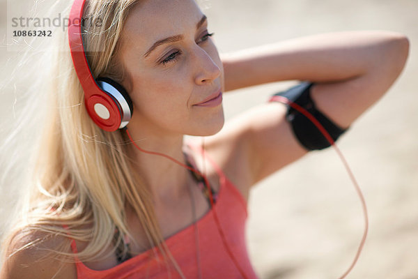 Junge Frau im Freien  mit Kopfhörern und Aktivitäts-Tracker
