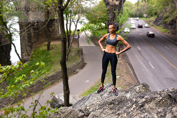 Frau in Sportkleidung steht auf Felsen über der Autobahn