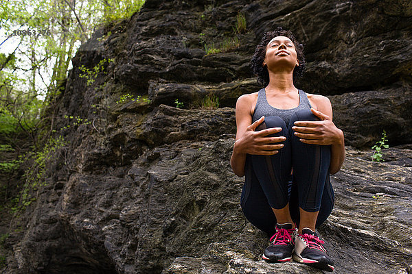 Frau sitzt kniend auf Felsen und meditiert