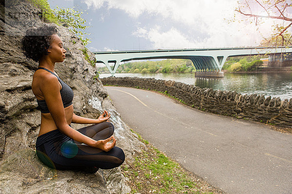 Frau sitzt im Schneidersitz auf einem Felsen und meditiert