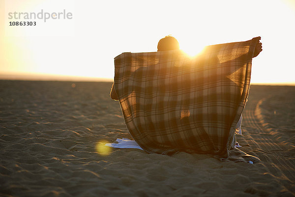 Ehepaar am Strand  bei Sonnenuntergang  Mann legt eine Decke um sie