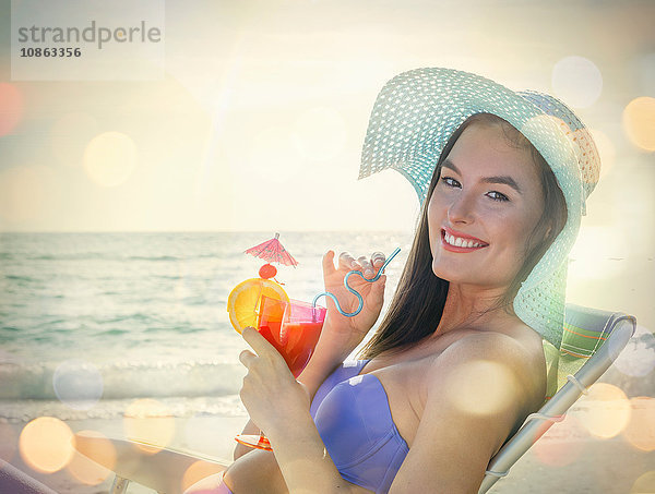 Porträt einer jungen Frau im Liegestuhl sitzend mit Cocktail am Strand von Miami  Florida  USA