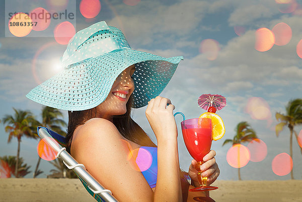 Junge Frau sitzt auf Liegestuhl mit Cocktail am Strand von Miami  Florida  USA