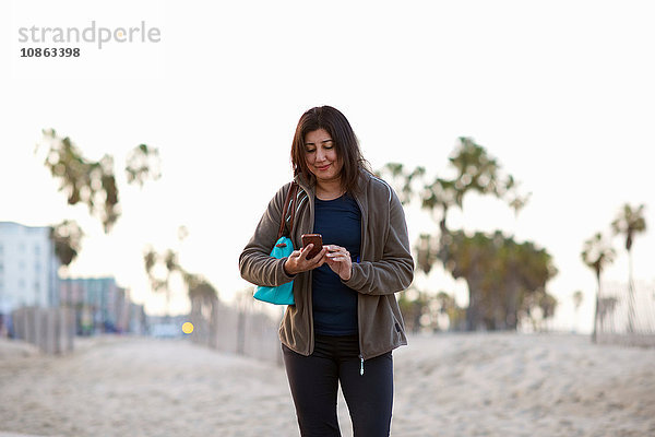 Frau mit Handtasche trägt Handtasche und schaut lächelnd auf Smartphone
