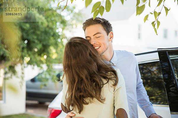 Junges Geschäftspaar küsst sich auf der Straße  bevor es mit dem Auto abfährt