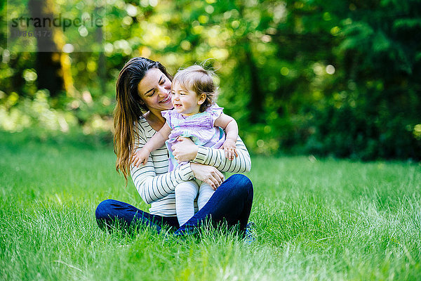 Frau umarmt Kleinkind-Tochter im Park