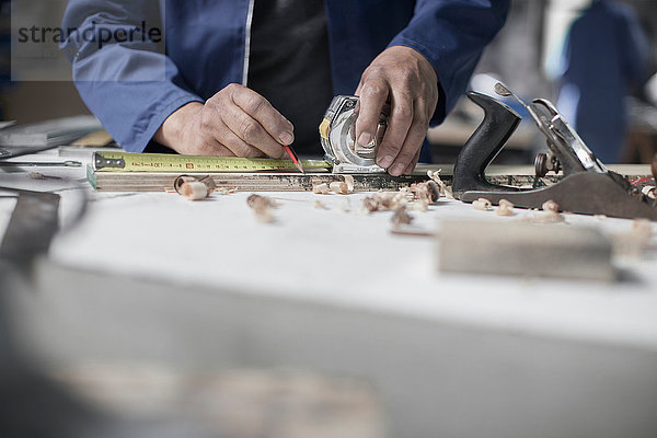 Schreinerhände messen Holz auf der Werkbank