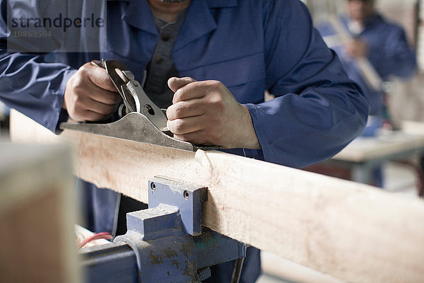 Tischlerhände mit dem Hobel auf dem Brett in der Werkstatt