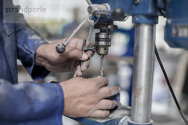 Nahaufnahme von Arbeiterhänden beim Anbringen des Bohrers in der Werkstatt