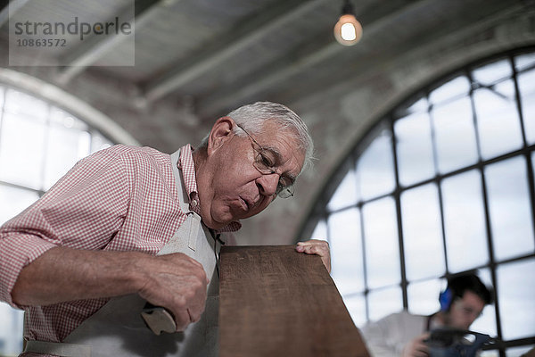 Leitender Zimmermann bläst Sägemehl von Holzbrettern in der Werkstatt