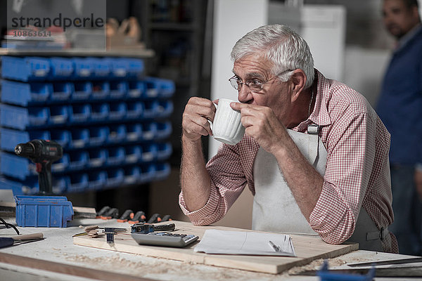 Senior-Tischler trinkt Kaffee in der Holzwerkstatt