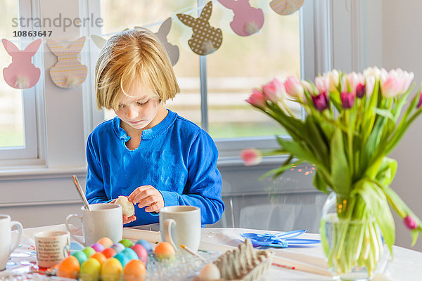 Junge am Tisch schmückt Eier für Ostern