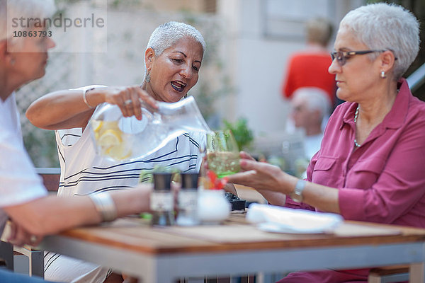 Ältere Frau und Freunde gießen Wasser im städtischen Straßencafé