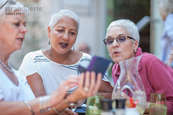 Ältere Frau und Freunde lesen Smartphone im städtischen Straßencafé