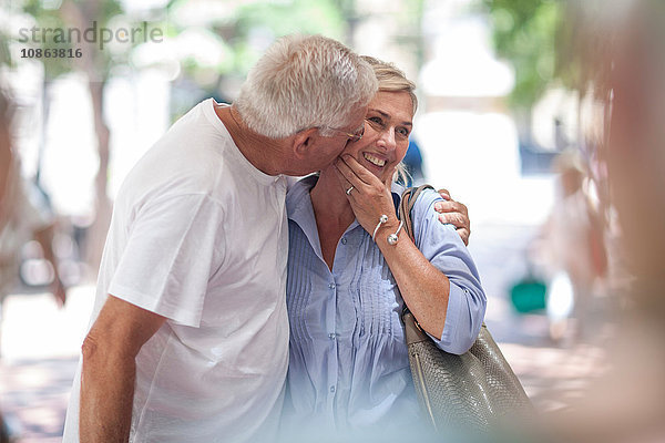 Älterer Mann küsst Frau in der Stadt auf die Wange