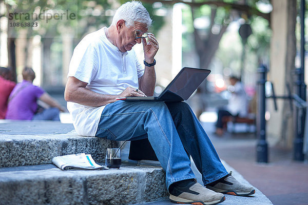 Älterer Mann mit Brille liest Laptop auf Stadttreppe
