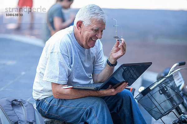 Älterer Mann auf Stadttreppe liest Laptop und lacht