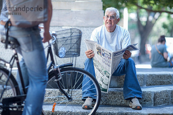 Älterer Mann auf Stadttreppe im Gespräch mit Radfahrer