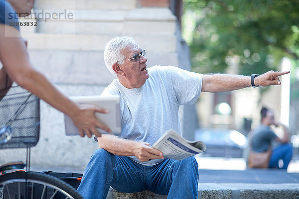Älterer Mann auf Stadttreppe lenkt Radfahrer mit digitalem Tablet