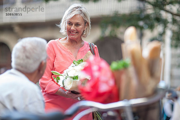 Frau zeigt einem älteren Mann in der Stadt einen Blumenstrauss