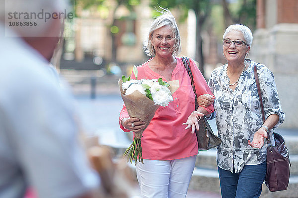 Zwei reife Frauen tragen einen Blumenstrauss Arm in Arm in der Stadt