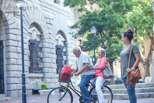 Junge Frau beobachtet älteren Mann und Frau beim gemeinsamen Radfahren in der Stadt