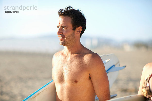 Männlicher Surfer mit nacktem Oberkörper und Surfbrett am Strand von Venice Beach  Kalifornien  USA