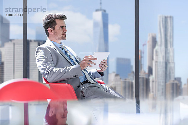 Junger Geschäftsmann benutzt digitales Tablet vor dem Fenster der New Yorker Skyline  USA