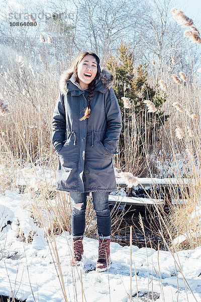 Ganzfigur einer Frau im Wintermantel in verschneiter Landschaft  die lächelnd in die Kamera blickt