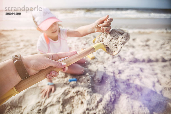 Persönliche Perspektive der Mutter am Strand  die eine Sandschaufel für ihre Tochter hält