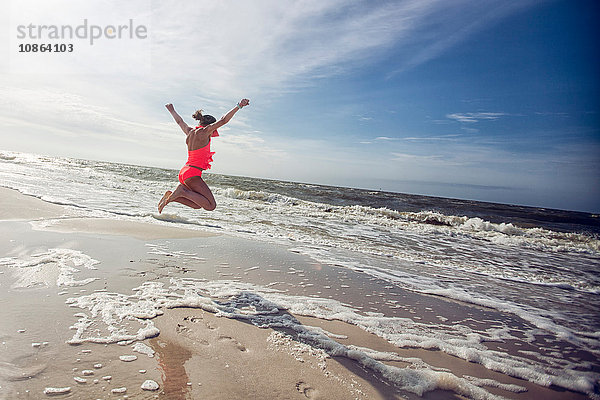 Seitenansicht eines Mädchens am Strand mit erhobenen Armen  das in die Luft springt