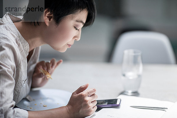 Frau benutzt Smartphone beim Essen