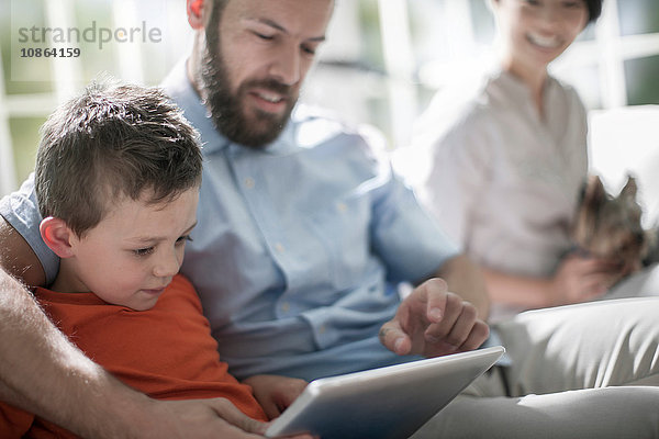 Vater und Sohn mit digitalem Tablett  Mutter mit Hund im Hintergrund