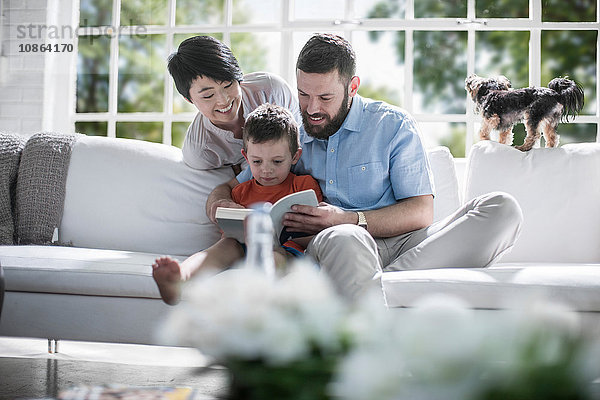 Ehepaar unterrichtet Sohn beim Lesen eines Buches auf dem Sofa