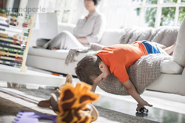 Junge spielt auf Sofa  Mutter im Hintergrund