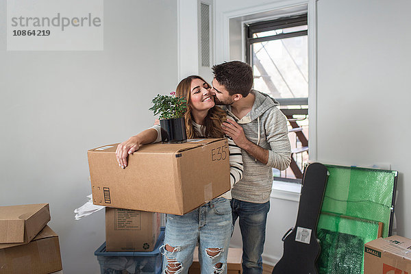 Umzug: junge Frau trägt einen Pappkarton  junger Mann küsst sie auf die Wange