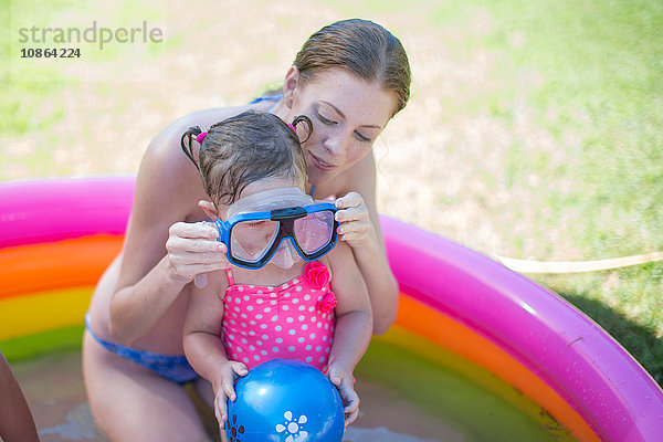Mutter setzt der Tochter im aufblasbaren Schwimmbecken eine Schutzbrille auf