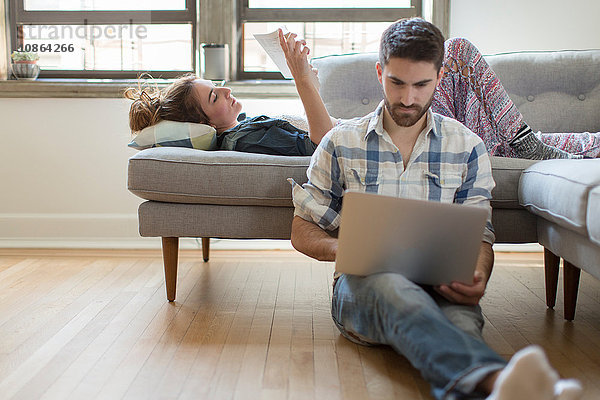 Junges Paar entspannt sich zu Hause  junge Frau liest Buch  junger Mann benutzt Laptop