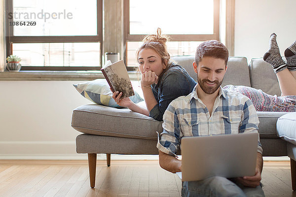 Junges Paar entspannt sich zu Hause  junge Frau liest Buch  junger Mann benutzt Laptop
