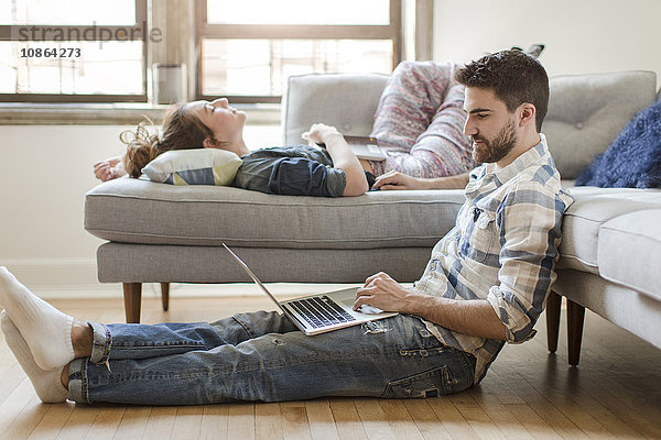 Junges Paar entspannt sich zu Hause  junge Frau schläft auf dem Sofa  junger Mann benutzt Laptop
